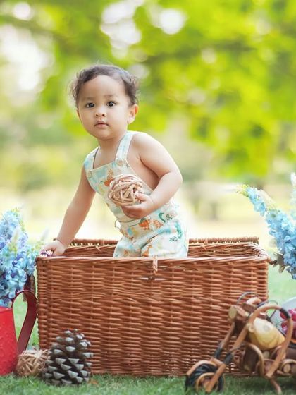 A beautiful outdoor baby portrait in a park. The wicker basket and flowers add a charming touch to the natural scenery.