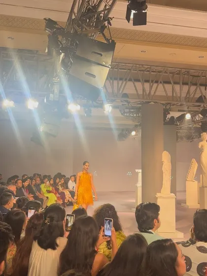 The audience watches as a vibrant orange design graces the runway. It's a privilege to be part of the ecosystem that brings these creative visions to life.