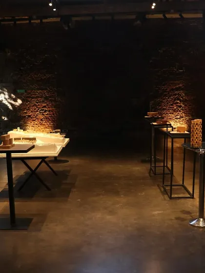 An empty exhibition hall at IF.BE, with models spotlit against the dark, textured walls. The atmosphere of the space itself, with its history and character, plays a crucial role in how the work is perceived.