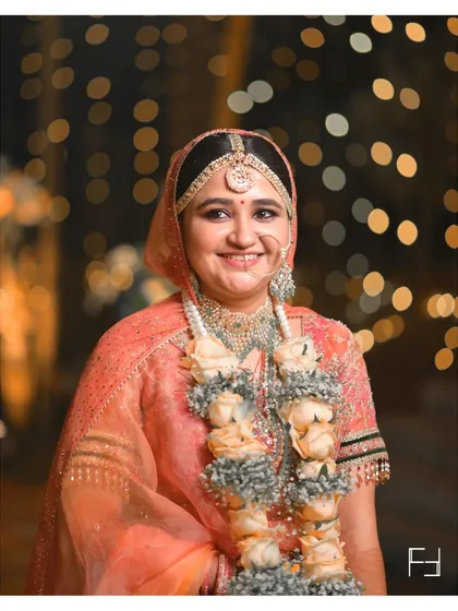 A close-up portrait of Nidhi, her face lit by the warm glow of the wedding lights. Her happy, natural smile is the centerpiece of this beautiful bridal shot.