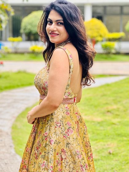 Amulya smiling in her floral brocade gown, a perfect fusion of traditional fabric and a modern, backless silhouette.