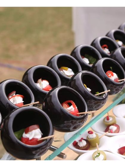 A close up of our mini caprese skewers, with cherry tomatoes, mozzarella, and basil, served in unique, modern black bowls. This is a simple classic, elevated by its presentation.