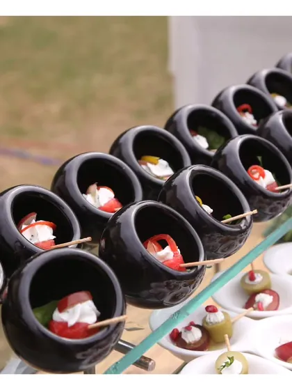 A close up of our mini caprese skewers, with cherry tomatoes, mozzarella, and basil, served in unique, modern black bowls. This is a simple classic, elevated by its presentation.