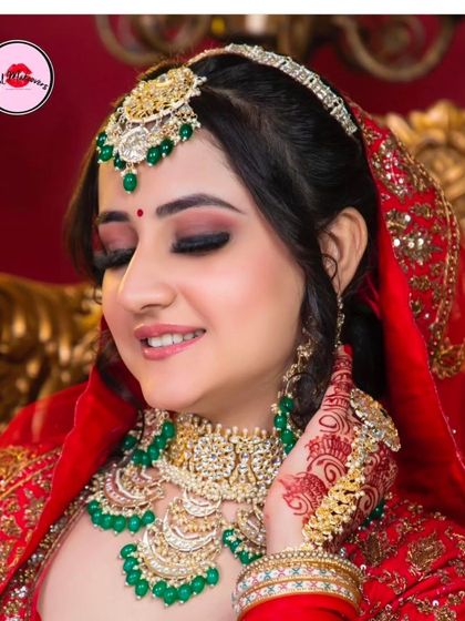 A happy bride with her eyes closed, wearing a lovely green-beaded Kundan set. The intricate hathphool with mehndi-adorned hands creates a perfect bridal picture.