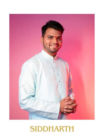 A classic portrait of the groom on his engagement day. Dressed in a light blue kurta, his warm smile and confident posture are captured against a simple, colorful backdrop.