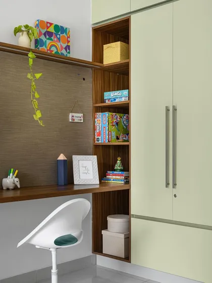 The study area in the 'Poorna' kid's room is integrated with the wardrobe. It features a spacious desk with a pin-up board and open shelving for books and supplies.