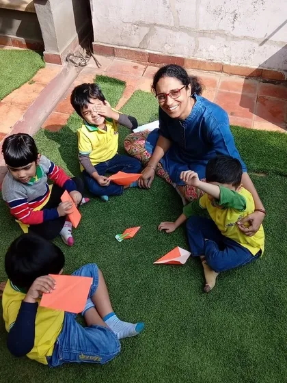 Learning happens everywhere, especially outdoors. Here, our children are enjoying an origami session in the sunshine, combining the fine motor skills of paper folding with the benefits of fresh air and natural light.