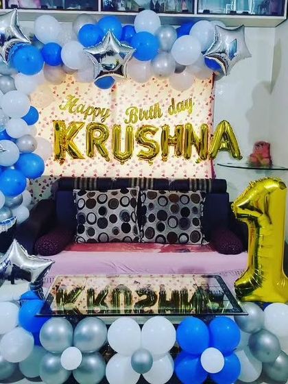 A vibrant first birthday home decoration in blue, silver, and white, with foil name balloons and a large number '1'.