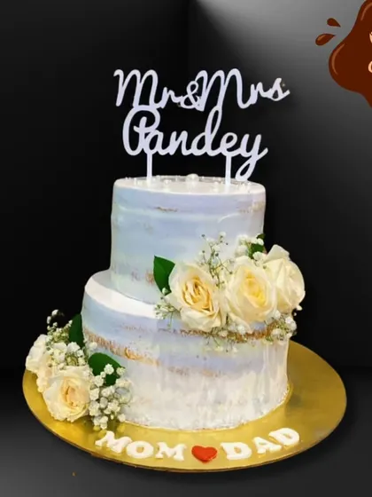 A simple yet elegant two-tier anniversary cake for "Mom & Dad." The semi-naked finish with white roses provides a rustic charm, showing that love and celebration can be both beautiful and understated.