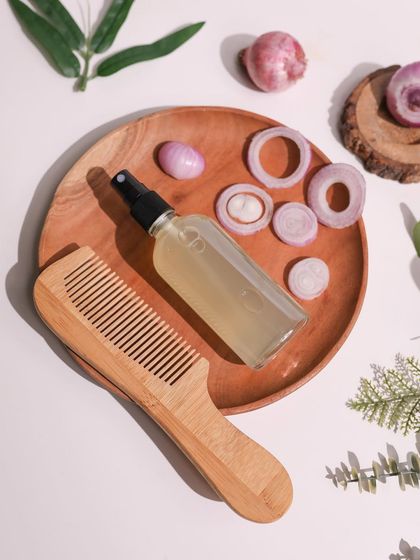 A flat-lay of a DIY onion hair spray with a wooden comb and fresh onion slices. The composition is clean and clearly communicates the key ingredient of the hair care recipe.