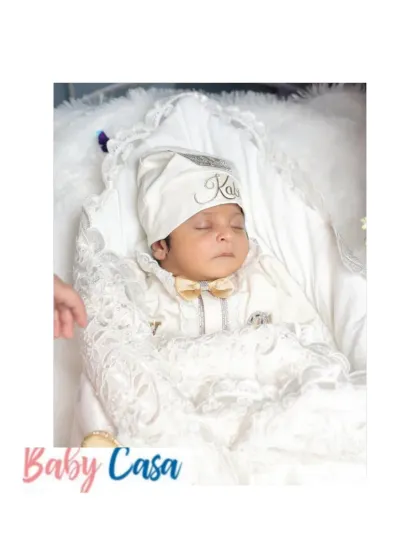 A precious moment of peace. This newborn is sleeping soundly in a custom all white coming home outfit, complete with a personalized cap and a beautifully detailed wrap.