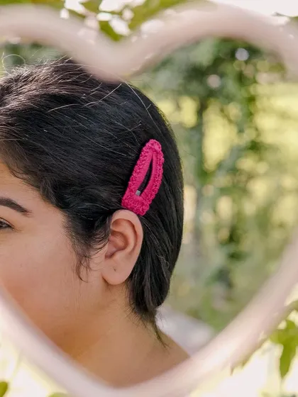 A close-up of a pink crochet hair clip, seen through a heart-shaped mirror. A simple way to add a pop of color and handmade charm.