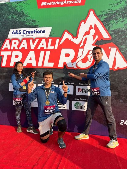Three runners celebrating at the finish line backdrop of the Aravali Trail Run, pointing to their success.