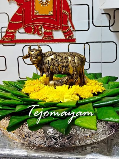 A beautiful offering for a housewarming ceremony, featuring a brass Kamadhenu statue on a bed of betel leaves and fresh flowers.