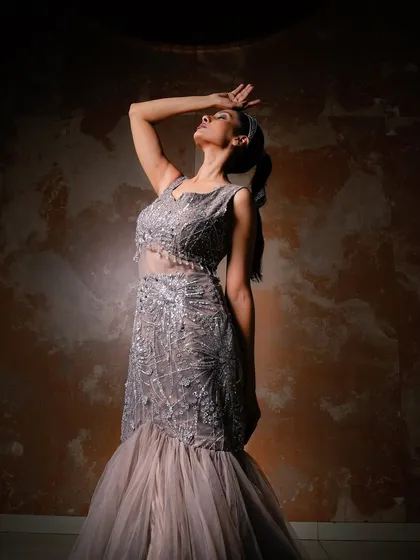 A dramatic, high-fashion pose in a grey gown. The upward gaze and strong lighting create a powerful and aspirational image, highlighting the model's profile and the shimmer of the dress.