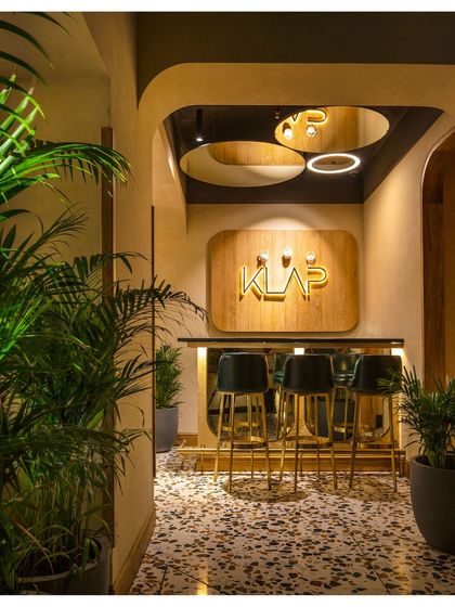 The entrance to a private dining area at Klap features a smaller, secondary bar. The space is defined by its curved entryway, warm wood signage, and circular mirrors on the ceiling that add a sense of illusory depth.