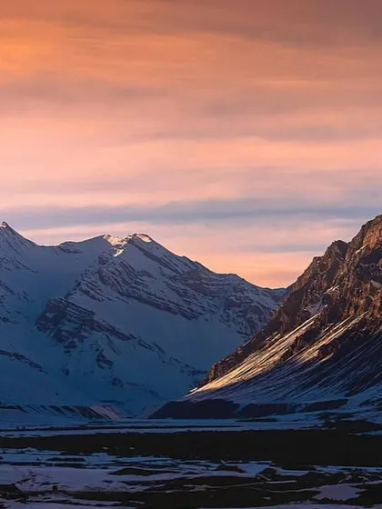 The soft pink and orange hues of a winter sunset over the Spiti mountain range. The light hits the snow-capped peaks in a way that's just pure magic.