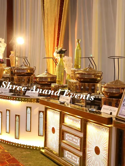 A close-up of a beautifully lit buffet counter where the warm glow highlights the intricate designs on the counter and the polished shine of the traditional brass serving pots. This setup is perfect for a classic, elegant wedding theme.