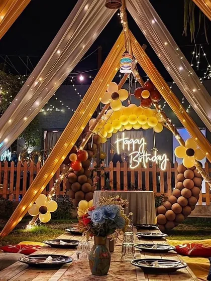 A beautiful outdoor birthday celebration featuring a canopy tent with elegant drapes, fairy lights, and low seating with cushions for a cozy, magical evening.