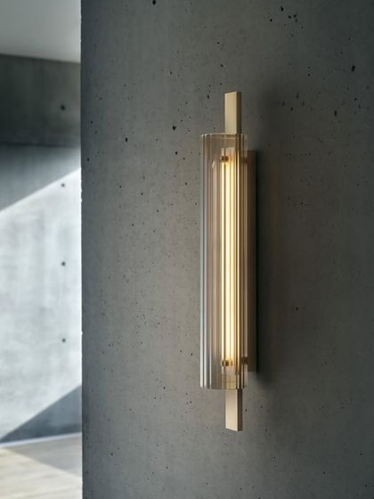 The Volant wall sconce, with its textured glass and solid brass bar, provides elegant and functional light against a concrete wall.