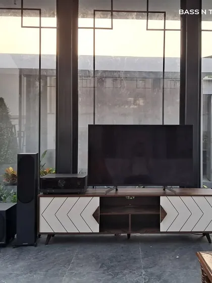 This entertainment den features Monitor Audio Bronze tower speakers and a subwoofer, creating a powerful soundstage for both movies and music. The system is designed to complement the modern interior of the glass-enclosed space.