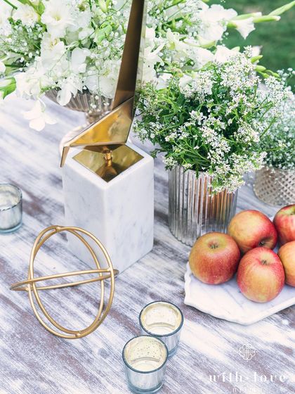 A table setting detail with apples and gold geometric objects. We often incorporate unexpected elements to add a layer of intrigue and personality to our designs.