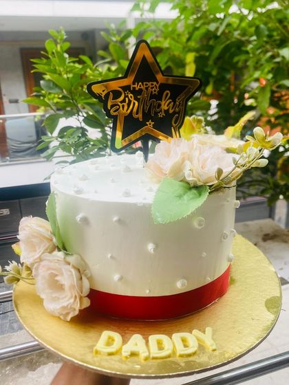An elegant birthday cake for "Daddy" with white roses and a gold star topper.