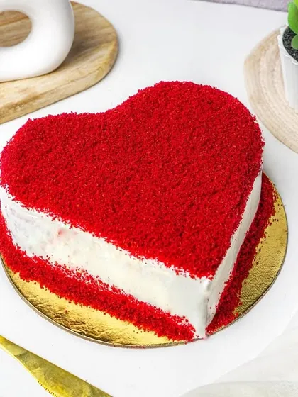 A heart-shaped red velvet cake styled with golden cutlery and a white cloth. This elegant setup is great for marketing specialty cakes for celebrations.
