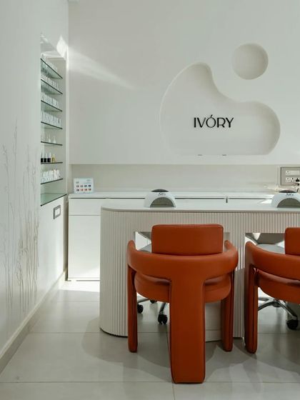 'The Ivory' nail salon by Studio Mudh features a clean, minimalist design with a custom-designed reception desk and bold orange chairs.