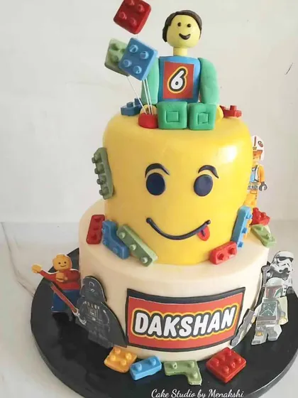 This two-tier Lego themed cake was built for fun, using very little fondant to keep it delicious. The design features a giant Lego head, colorful bricks, and characters from the universe, all handcrafted for the birthday boy.