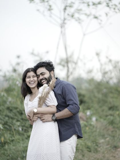 A joyful, candid embrace in a field, with the couple laughing, showcasing their natural chemistry.
