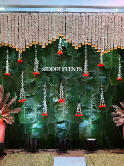 We love blending natural elements with traditional florals. This unique stage backdrop features a wall of fresh green banana leaves, beautifully contrasted with hanging curtains of white and red tuberose, offering a touch of South Indian elegance to the celebration.