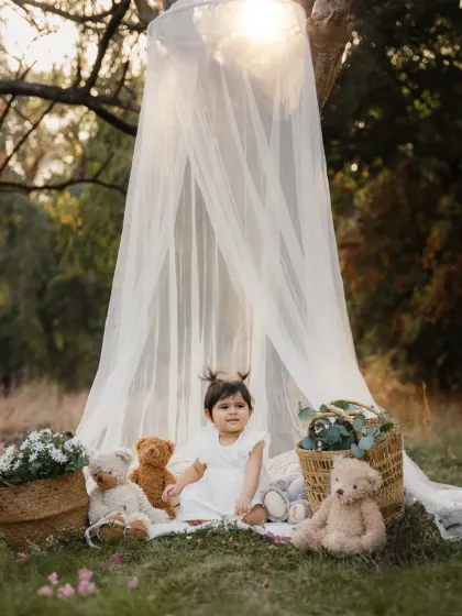 A little girl sits in a dreamy outdoor teepee setup, surrounded by teddy bears. This whimsical scene is perfect for a toddler photoshoot.