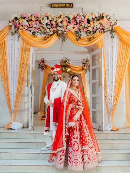 A classic portrait of the bride and groom, perfectly framed by the floral decor of their wedding hall. This is a timeless shot that captures the elegance and grandeur of a classic Indian wedding.