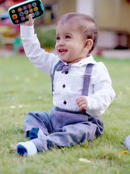 A smiling toddler holds up a toy phone, a fun and modern portrait from an outdoor session.