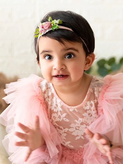 An expressive baby girl in a frilly pink dress claps her hands during her sitter session.
