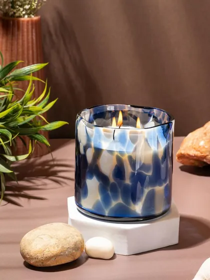 A styled lifestyle shot of a Lighthouse candle, using natural elements like stone and plants to create a serene, earthy mood. The focus is on showing how the home decor product fits into a calming personal space.