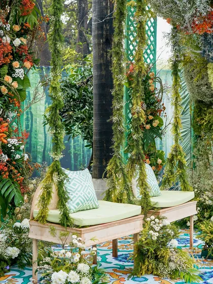 A wider view of the moss-draped floral swing, showing how it is nestled within a lush, green, forest-like environment.