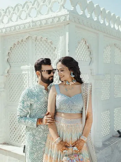 A stylish portrait of the couple in front of a white, intricately designed wall, their modern sunglasses adding a cool touch.