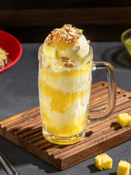 A pineapple sundae in a glass mug, with layers of ice cream, fruit, and nuts.