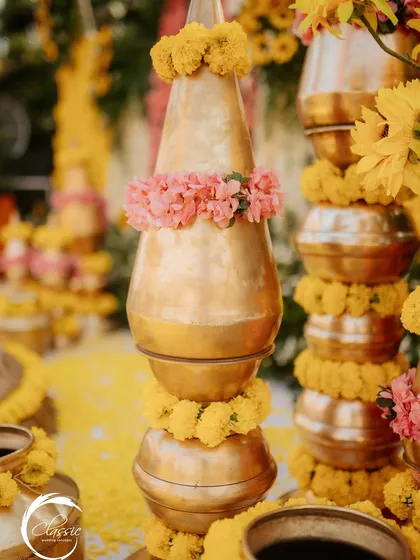 Detail is key. This is a close-up of a stacked brass matka, where each layer is carefully adorned with marigold garlands and a delicate band of pink flowers.
