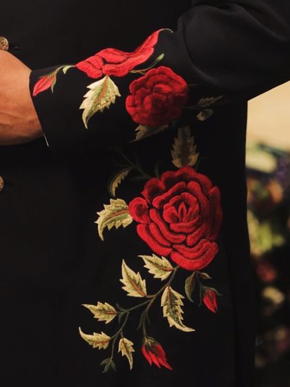 A close-up of the intricate red rose embroidery on the sleeve of the navy sherwani. This level of detailed craftsmanship is what makes our bespoke traditional wear truly special.