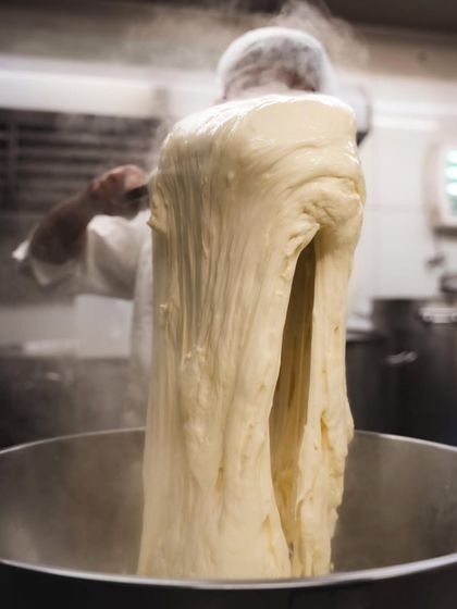 A massive stretch of mozzarella being pulled from the whey, demonstrating the incredible elasticity of our handmade cheese.