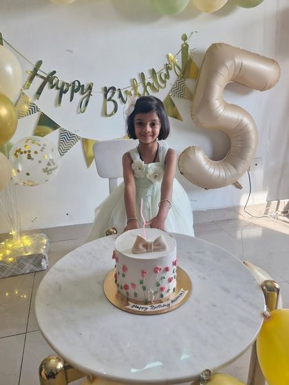 A client photo showing our simple and sweet spring-themed cake at a 5th birthday party. The cake features a fondant bow and delicate piped pink flowers.