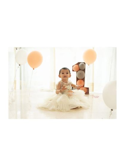 Looking up with curiosity. This candid moment was captured during a first birthday shoot, surrounded by soft peach and white balloons.