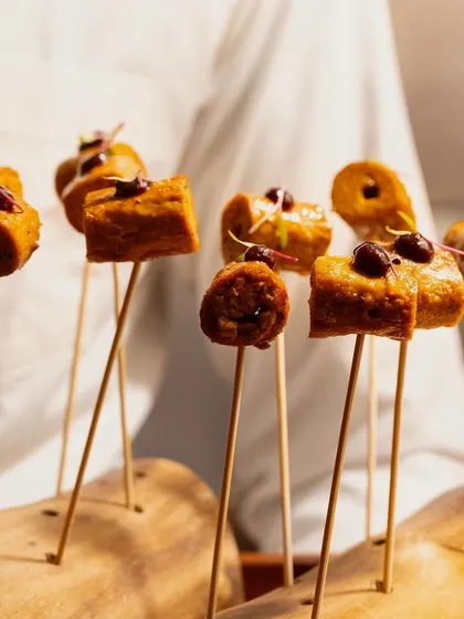 A chef presents a wooden platter of our savory kebab skewers, a highlight from our Modern Indian canapé selection.