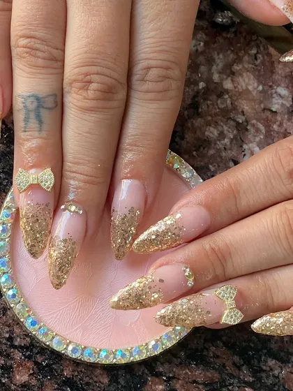 A glamorous gold glitter ombre set on stiletto nails, with sparkling 3D rhinestone bows.