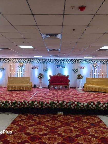 A wide stage setup for a large wedding reception. It features a central royal sofa for the main couple, flanked by two additional sofas for family, all set against a beautifully lit backdrop with floral accents.