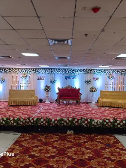 A wide stage setup for a large wedding reception. It features a central royal sofa for the main couple, flanked by two additional sofas for family, all set against a beautifully lit backdrop with floral accents.