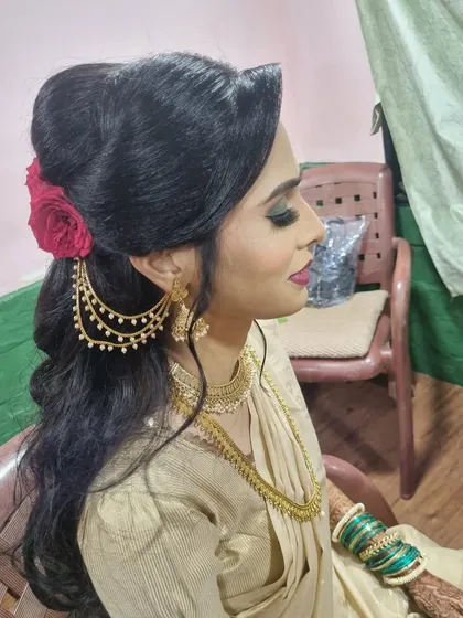 A side profile of a gorgeous reception look. The hairstyle is a soft, open-curl look accessorized with a rose and traditional jewelry.